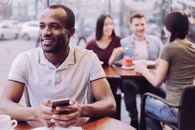 Energetic hopeful pensive man holding phone while staring aside and posing at cafe