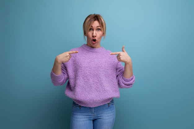 Energetic indignant blond young woman in purple hoodie screaming in surprise on a blue background