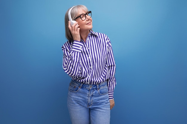 Energetic retired woman with gray hair getting acquainted with gadgets for music on a bright studio