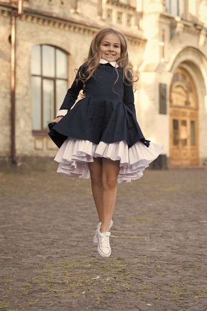 Energetic small kid in elegant uniform dress jump in school yard outdoors schooling