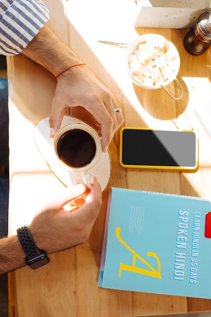 Energizing drink. Top view of a coffee cup in male hands while sitting at the table