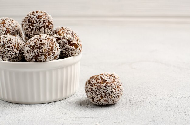 Energy balls of dates, nuts, oats, sprinkled with coconut powder closeup in a white plate on a white table