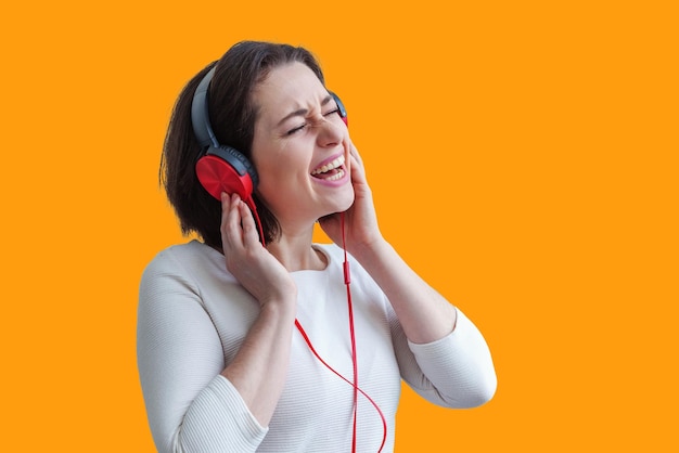 Energy young brunette lady woman listening music in headphones and singing isolated on yellow background Charming caucasian girl in earphones enjoying music and dancing with closed eyes