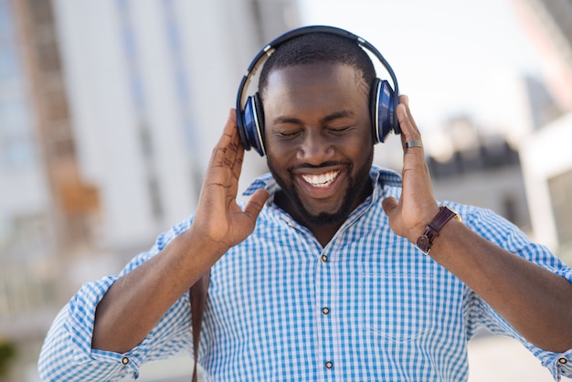 Engaging cool excited guy wearing cool headphones and listening to his favorite song while having a moment for relaxation