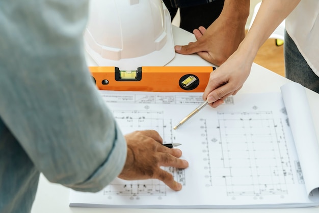 Engineer, architect, construction worker team working and pointing on drawing blueprint on workplace desk in meeting room office at construction site, contractor, teamwork, construction concept