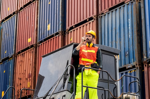 Engineer beard man standing with ware a yellow helmet to control loading and check a quality of containers from Cargo freight ship for import and export at shipyard or harbor