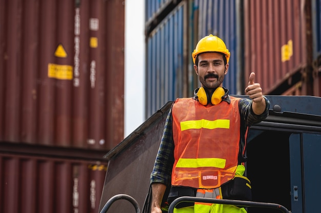 Engineer beard man standing with ware a yellow helmet to control loading and check a quality of containers from Cargo freight ship for import and export at shipyard or harbor