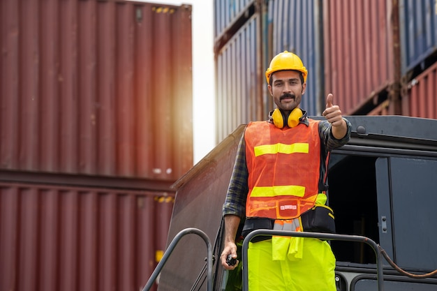 Engineer beard man standing with ware a yellow helmet to control loading and check a quality of containers from Cargo freight ship for import and export at shipyard or harbor