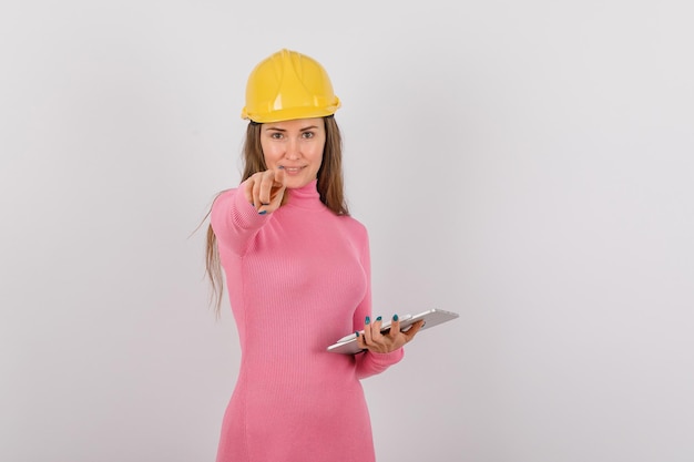 Engineer girl with tablet computer is pointing to camera with forefinger on white background