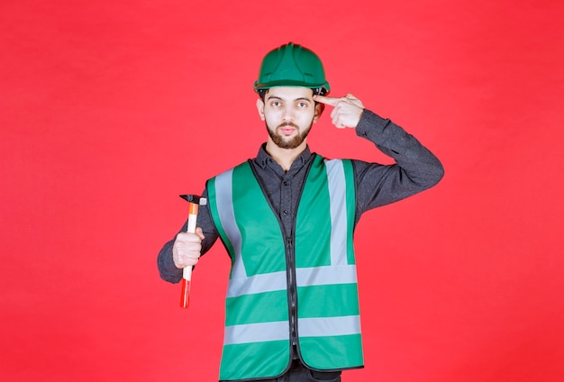 Engineer in green uniform and helmet holding a wooden ax and thinking. 