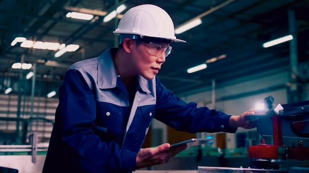 Engineer is using a tablet to check the machine's control system in a factory.