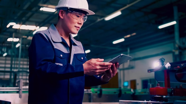 Engineer is using a tablet to check the machine's control system in a factory.