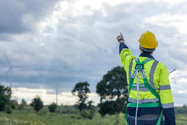 Photo engineer male working in wind turbines farm back view hand pointing at the sky for future of eco clean energy worker people