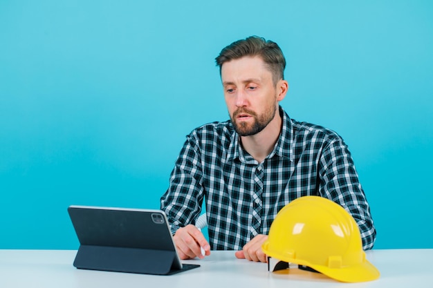 Engineer man is sitting in front of his tablet on blue background