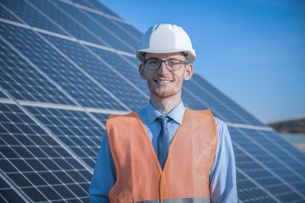 Engineer, man in uniform, helmet glasses and work jacket on a background of solar panels at solar station