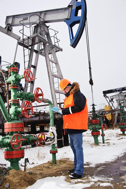 Engineer in orange uniform and helmet on of background the pump jack.