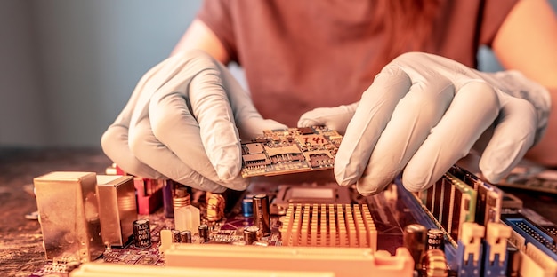 Engineer's gloved hand holds the chip board on the background of the motherboard Hightech hardware microelectronics