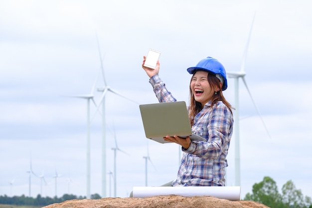 An engineer sits at his laptop looking at a clean energy wind turbine project to generate electricity.