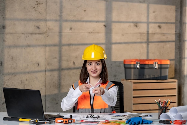 Engineer smart young cute brunette girl civil worker in helmet and vest pointing at you