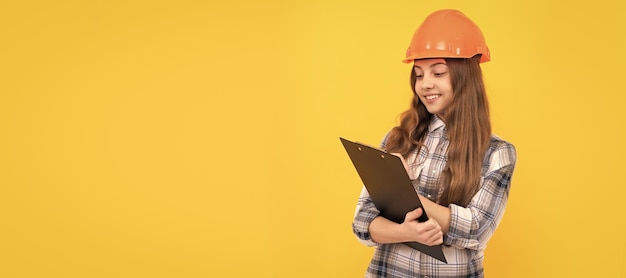 Engineer teenager girl happy teen girl in helmet and checkered shirt making notes on clipboard make notes Child in hard hat horizontal poster design Banner header copy space