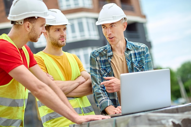 Engineer and two workers discussing near laptop outdoors