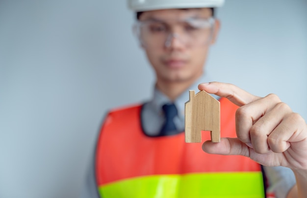 Engineer wears a reflective vest Glasses and helmets In his hand held a model of a wooden house