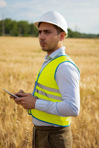 An engineer with a tablet in his hands stands in the middle of a field t checks the harvest