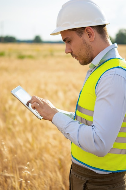 An engineer with a tablet in his hands stands in the middle of a field t checks the harvest