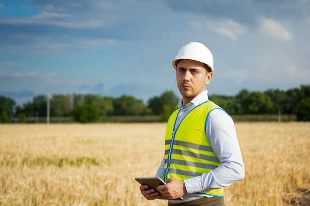 An engineer with a tablet in his hands stands in the middle of a field t checks the harvest