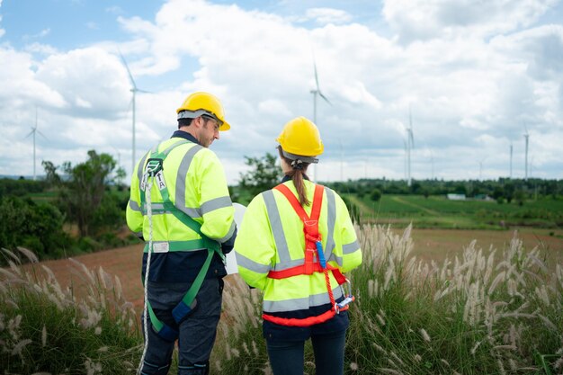 Photo engineer and worker discussing the project on the background of wind turbines