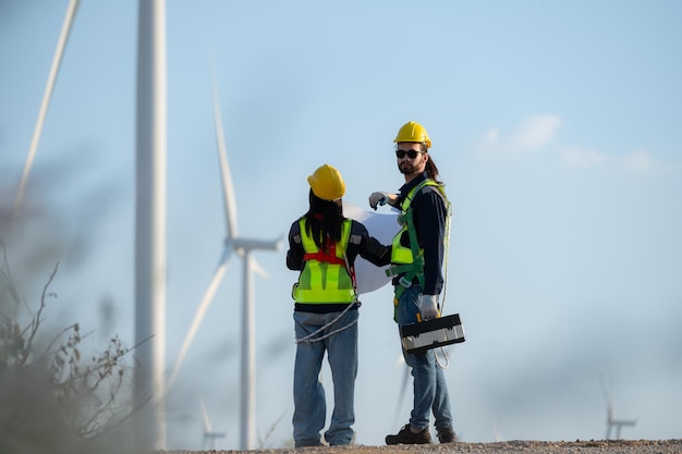 Photo engineer and worker discussing on a wind turbine farm with blueprints