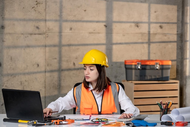 Engineer young cute smart brunette girl civil worker in helmet and vest on computer