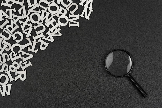 English alphabet letters and magnifying glass on black background Search for words and information concept