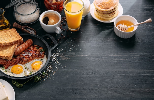 English breakfast on a dark table fried eggs with bacon canned beans and sausage