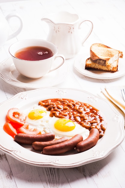 English breakfast - eggs, sausages with beans and tea with milk