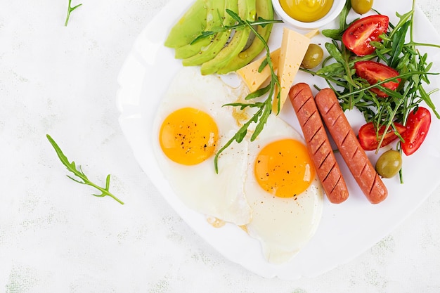 English breakfast fried eggs sausages tomatoes avocado cheese and olives American food Top view overhead copy space