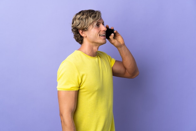 English man over isolated purple background keeping a conversation with the mobile phone