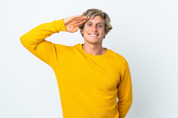 English man over isolated white wall saluting with hand with happy expression