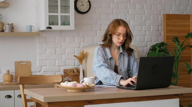 Photo engrossed in her work a woman writes in a notebook while using a laptop in a bright kitchen this