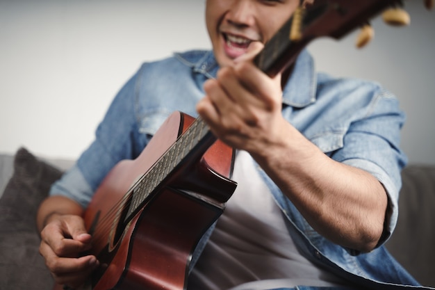 Enjoy handsome asian man practicing or playing the guitar on the sofa at living room