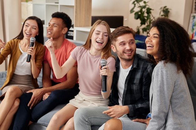 Enjoy with music smiling friends looking excited while playing karaoke at home singing with