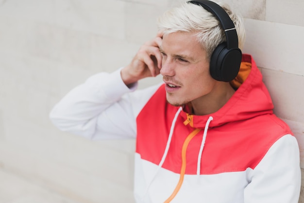 Enjoying attractive portrait of young male dressed in red sportswear resting after physical activities in open air in parkYoung handsome man listening to music with headphones against grey background