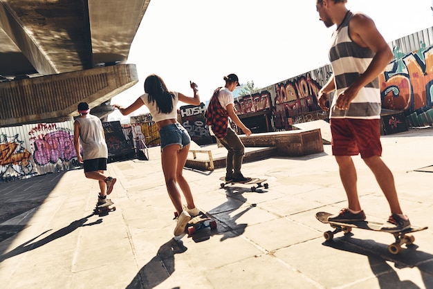 Enjoying carefree time together. Group of young modern people skateboarding together outdoors