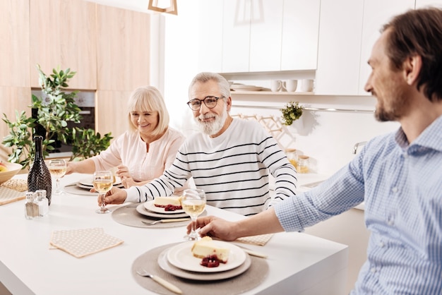 Enjoying cozy family dinner . Charismatic optimistic cheerful aged couple having dinner and enjoying weekend with their mature son while holding glasses full of champagne