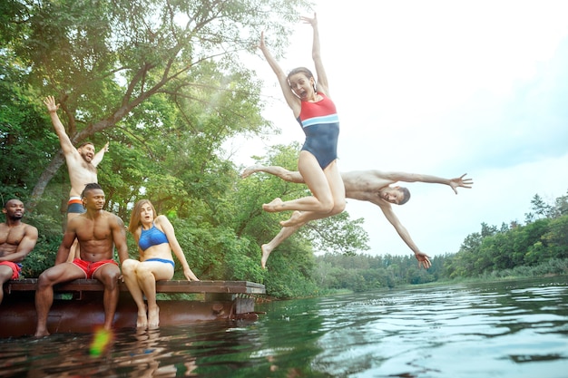 Enjoying forest party with friends. Group of beautiful happy young men and girls swimming at the river together. Summer, party, adventure, youth, frienship concept