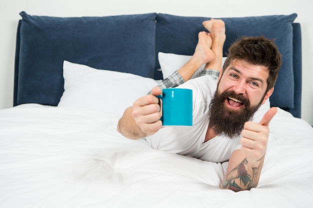 Enjoying fresh coffee happy bearded man hipster drink morning coffee brutal sleepy man in bedroom mature male with beard in pajama on bed asleep and awake energy and tiredness Fresh coffee