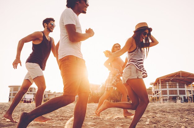 Enjoying fun time together. Group of young cheerful people running along the beach and looking happy