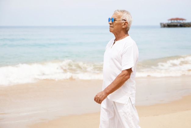 Enjoying the retirement. Happy senior man walking on the beach.