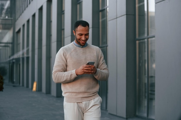 Enjoying social media by using smartphone Handsome black man is outdoors near the business building