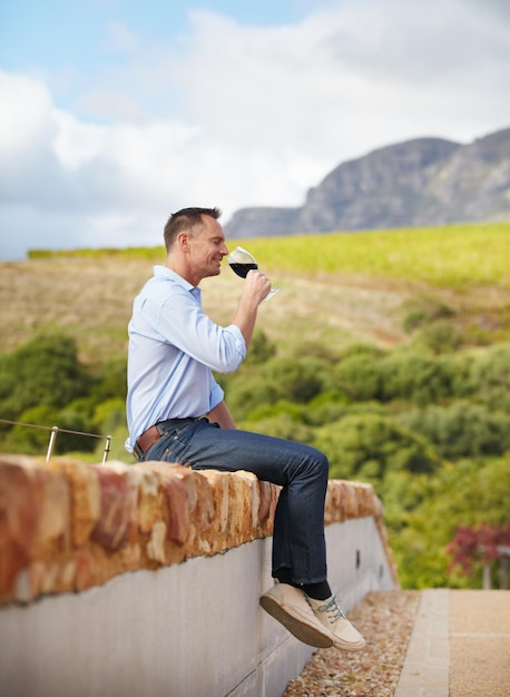 Enjoying some wine in the great outdoors A mature man sitting on wall and enjoying a glass of red wine